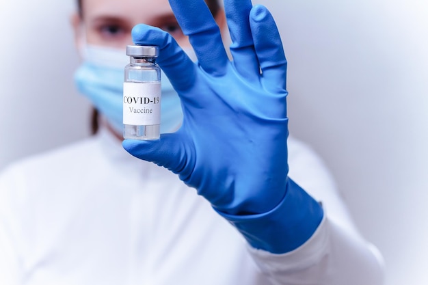 Closeup of a female doctor wearing a protective mask and blue gloves holding a bottle of COVID19 vaccine