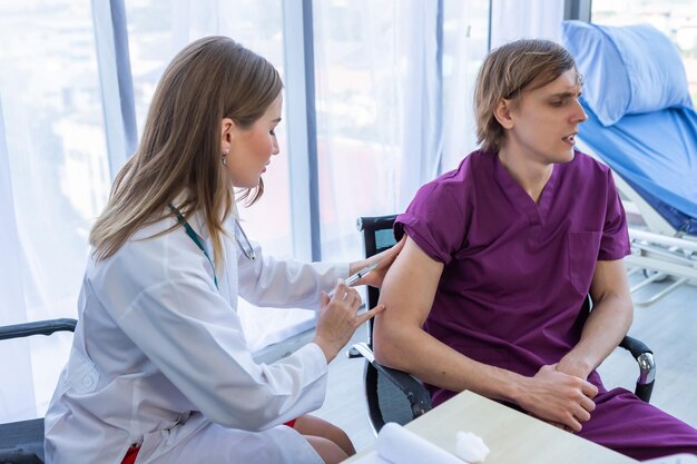 Closeup of female doctor with syringe to the arm of a man patient sit in a wheelchair for better healing In the room hospital background