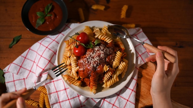Фото Женщина крупным планом ест вкусную итальянскую томатную пасту фузилли с вилкой и ложкой за винтажным обеденным столом