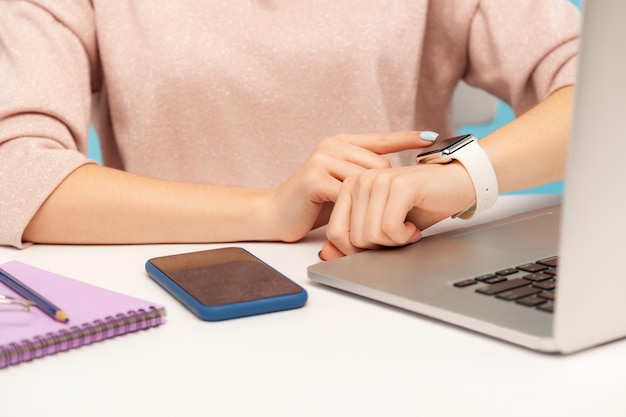 Closeup of female employee looking at smart watch on her hand while working on laptop in office, checking hour to take break, touching screen to turn off alarm clock. indoor studio shot, isolated