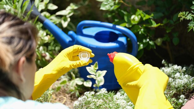 정원 가꾸기 개선에 물을 주기 위해 비료를 추가하는 여성 정원사의 클로즈업