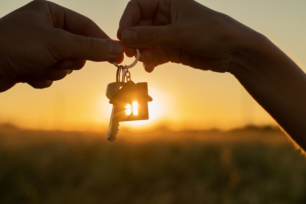 Closeup female gives a man the key to a new house on the background of a beautiful sunset the concep...