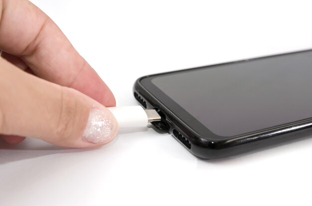 Closeup of female hand connecting the charging cable to the smartphone isolated on white background