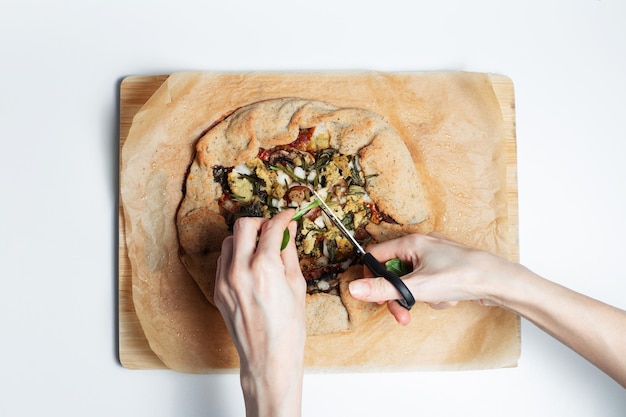 Closeup of female hand cutting greens above galette Homemade vegan food