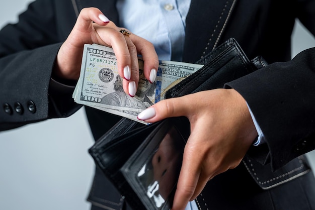 Closeup of a female hand holding a black wallet in which there\
are dollars woman with dollars money in wallet abundance