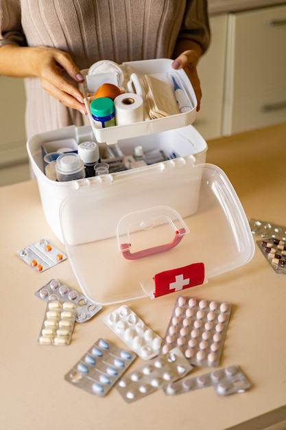 Foto mano femminile del primo piano che dispone il rifornimento di emergenza dell'organizzazione di stoccaggio del kit di pronto soccorso domestico del medicamento