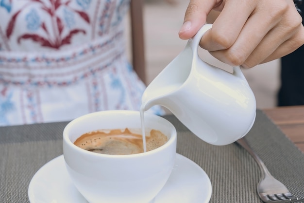 Closeup of female hand pouring hot milk foam into espresso