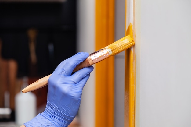 オレンジ色の塗料でペイントブラシ絵画天然木製ドアと紫のゴム手袋で女性の手をクローズアップ。色の明るい創造的なデザインのインテリア。木製の表面をペイントする方法。選択したフォーカス