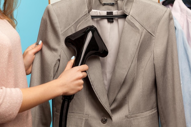 Closeup female hand steaming business suit at drycleaner advertisement of professional services washing cleaning and ironing clothes care of fabric indoor studio shot isolated on blue background