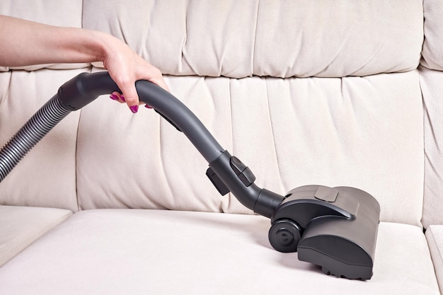 Closeup of a female hand vacuums the surface of the beige sofa