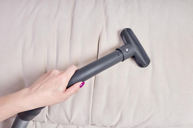 Closeup of a female hand vacuums the surface of the beige sofa