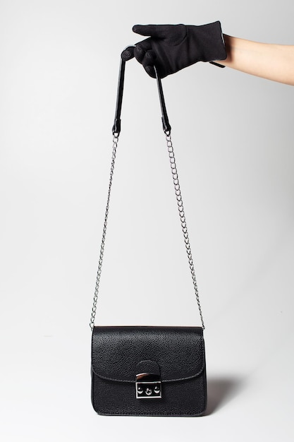 Closeup of female hand wearing black glove holding a woman small handbag by handle strap on white background