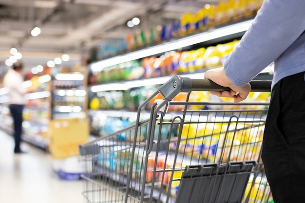 Closeup of a female hand with trolley cart shopping at supermarket