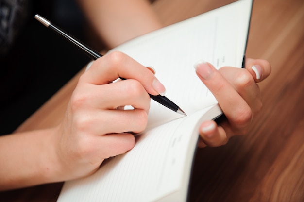 Closeup of a female hand writing on an blank notebook with a pen