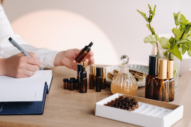 Closeup of female hands holding a bottle of essential oil and writing an entry in a notebook aromatherapy