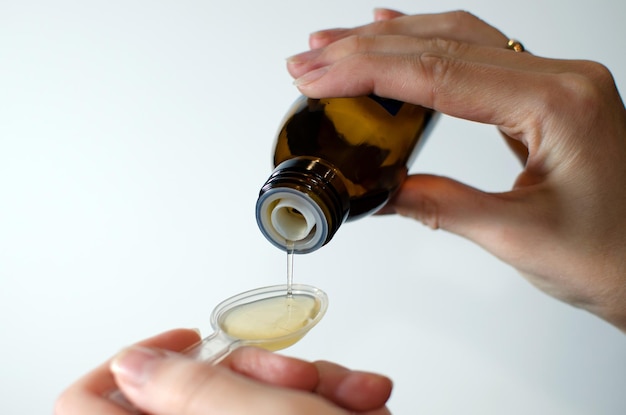 Closeup of female hands holding a bottle of expectorant cough syrup and pouring it with a measuring ...