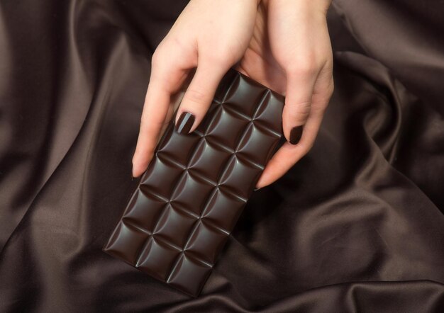 Primo piano delle mani femminili che tengono la barra di cioccolato fondente