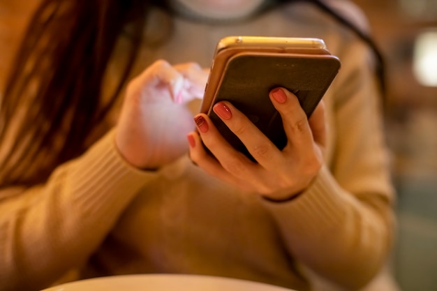 Closeup of female hands holding a phone and typing in it in the evening in a cafe