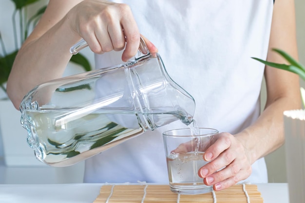健康のためのガラスの朝の儀式に飲料水を注ぐ女性の手のクローズアップ