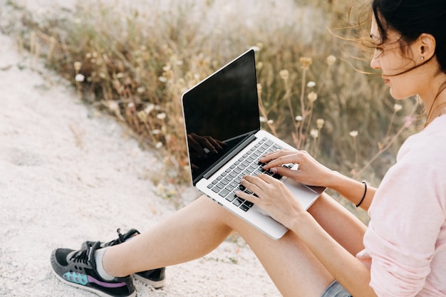 Closeup of female hands typing on laptop, outdoors, at a beach.