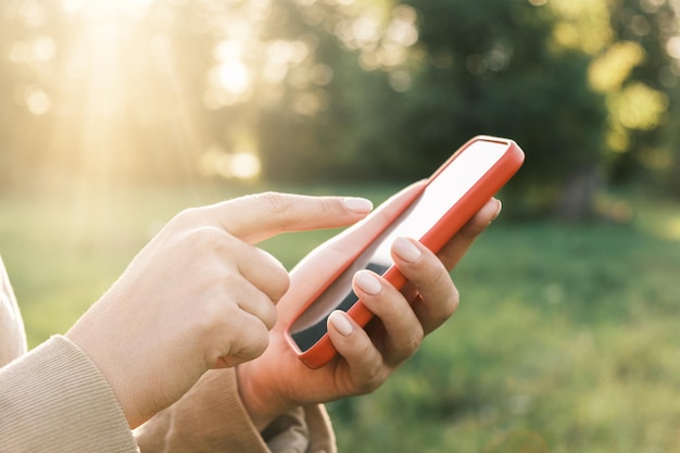 Closeup of female hands using a smart phone nature background Woman using mobile phone in sunset outdoors Unrecognizable person touching smartphone screen Unknown girl holding cellphone outside