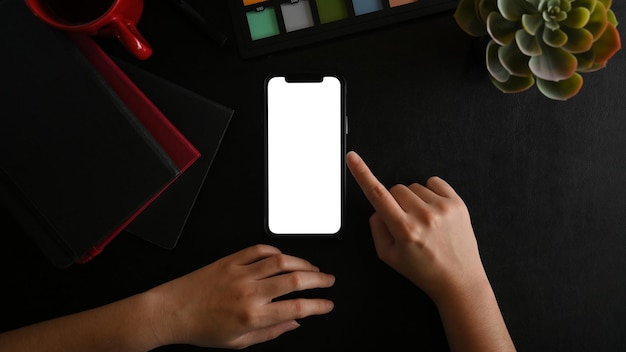 黒の背景の上面図にスマートフォンの空白の画面のモックアップを使用して女性の手をクローズアップ