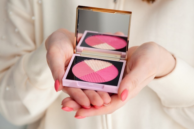 Closeup female hands with manicure holding corrective sculpting palette pink blush with mirror.