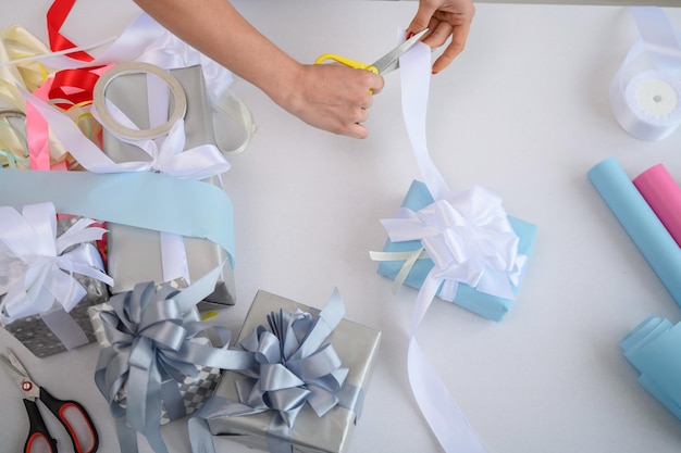 Closeup of female hands wrapping gifts for the new year Woman holds handmade christmas gift Preparation for the holiday Box with a bow Desktop with wrapping paper