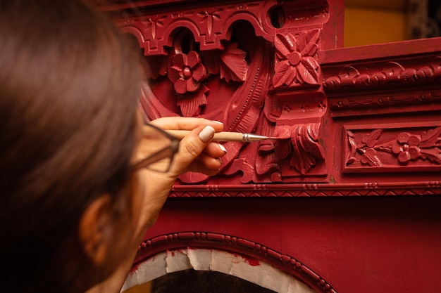 Primo piano di una donna con un pennello sottile in mano dipingendo con cura il vecchio armadio in colore rosso officina domestica per la ristrutturazione di mobili nuova vita per le cose vecchie