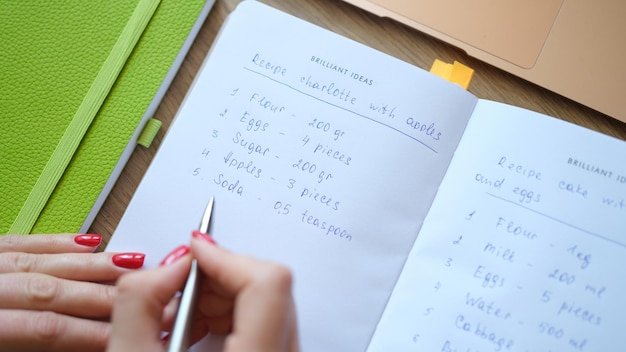 Closeup of female housewife writing down recipe of charlotte with apples cooking preparing food