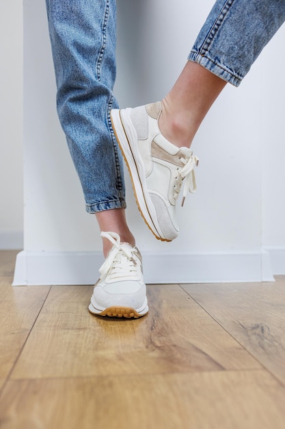 Closeup of female legs in jeans and casual sneakers Women's comfortable casual shoes White leather women's sneakers