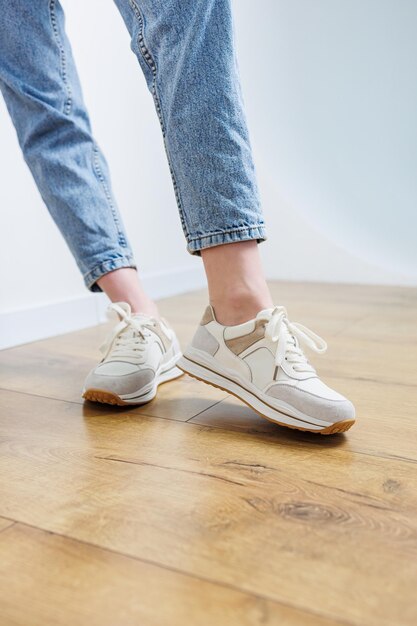 Closeup of female legs in jeans and casual sneakers Women's comfortable casual shoes White leather women's sneakers