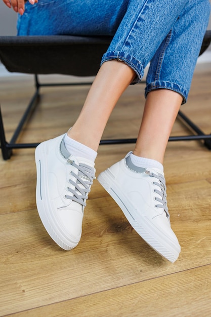 Closeup of female legs in jeans and casual white sneakers Women's comfortable casual shoes White leather women's sneakers