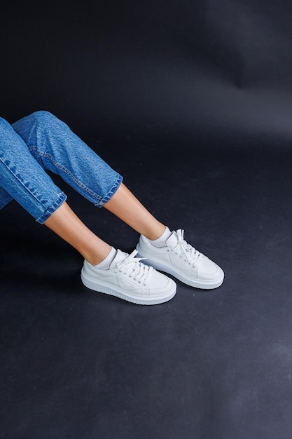 Крупный план женских ног в джинсах и повседневных белых кроссовках Женская удобная повседневная обувь Белые кожаные женские кроссовки