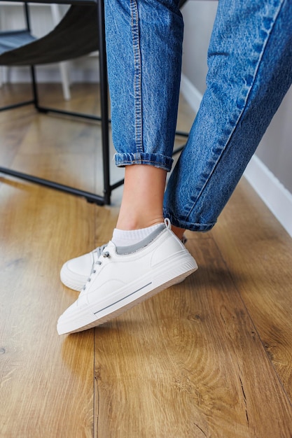 Closeup of female legs in jeans and casual white sneakers Women's comfortable casual shoes White leather women's sneakers