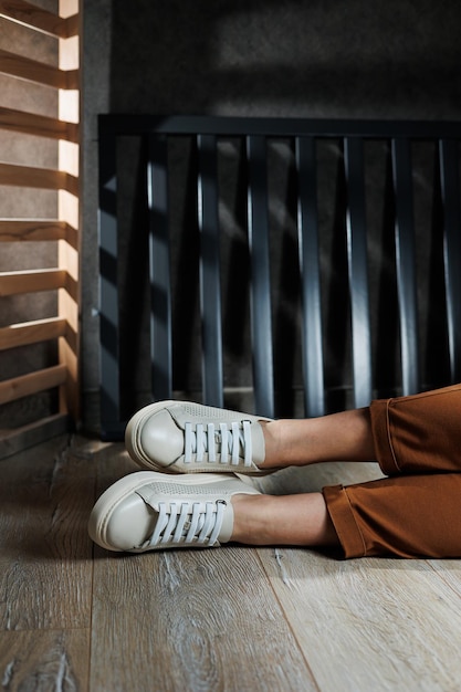 Closeup of female legs in leather white shoes Young woman standing in leather stylish white sneakers in brown pants Summer women's shoes Casual street style