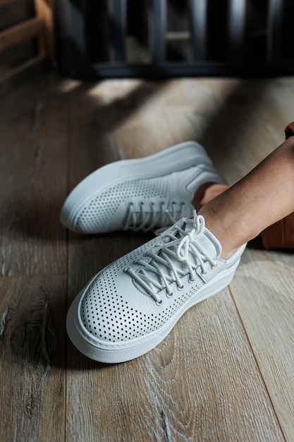 Closeup of female legs in white perforated leather sneakers Womens summer sneakers Collection of womens leather shoes