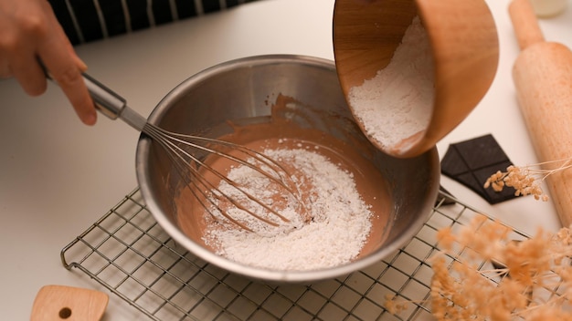 Closeup Female preparing a cookies dough adding a cup of flour into a mixing bowl in the kitchen