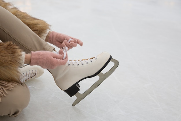 Foto primo piano della donna seduta sulla pista di pattinaggio sul ghiaccio e legare i lacci delle scarpe