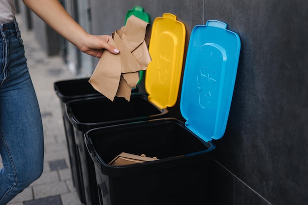 Крупным планом женщина бросает кусок картона в мусорное ведро разного цвета мусорных контейнеров