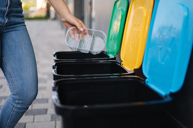 ごみ箱の異なる色のごみ箱にプラスチック容器を投げる女性のクローズアップ