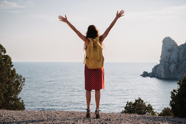 Closeup A female tourist with a yellow backpack standing with her hands up on the top The girl greets the sun