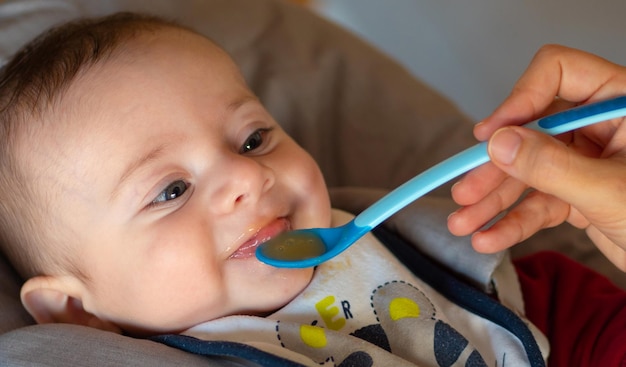 Primo piano di un bambino di pochi mesi che inizia lo svezzamento mangiando una purea di frutta