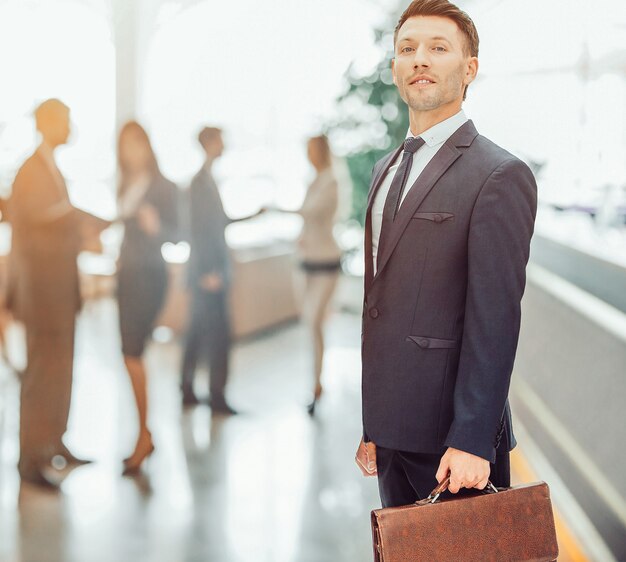 Closeup of a financial Manager in a black business suit with a briefcase on the background of office staff.the photo has a empty space for your text