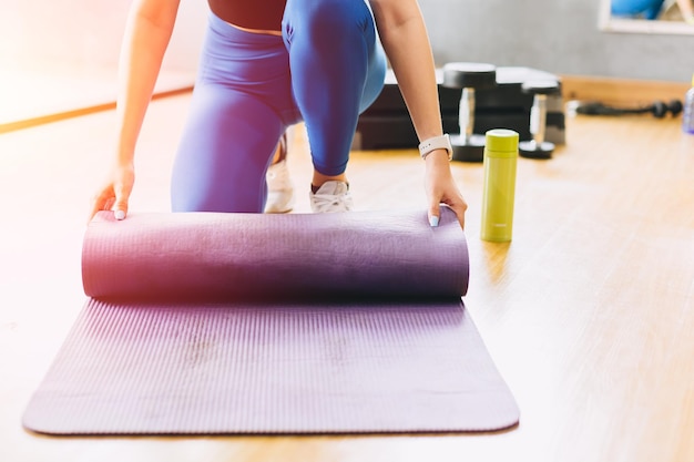 Closeup fitness woman in sport club studio with yoga mat Young woman roll pilates mat at a fitness training class