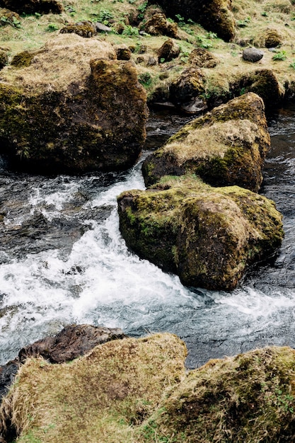 Крупный план потока воды зеленой горной реки, желтой травы и камней.