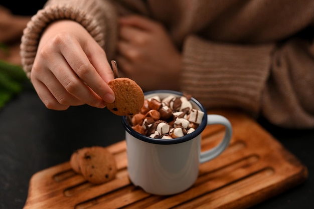 Closeup Focus hands Female dripping soft cookie into a hot chocolate with marshmallows Hot drink