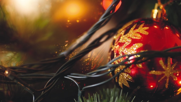 Closeup footage red ball with golden glitter hanging on Christmas tree against glowing light garland