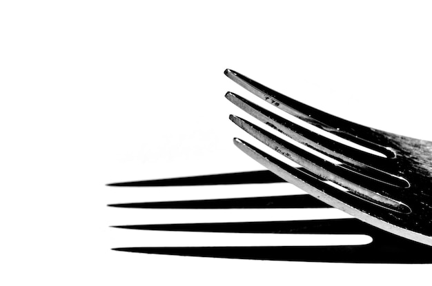 Closeup of a fork horizontally on a white surface, with a harsh shadow.