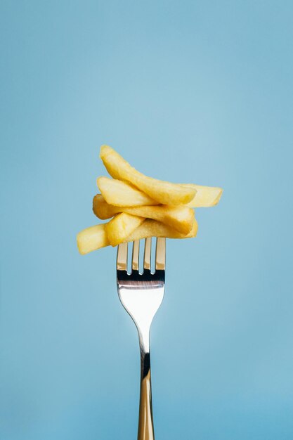 Foto primo piano di patatine fritte tritate su una forchetta su sfondo blu